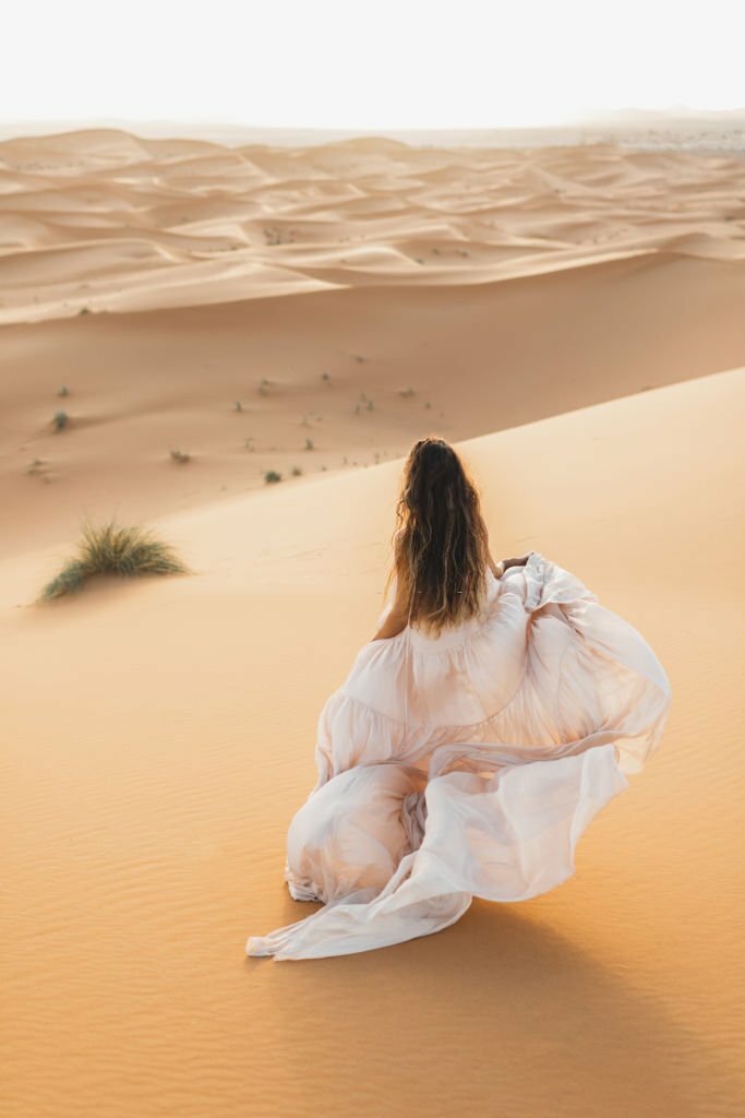 Portrait of bride woman in amazing wedding dress in Sahara desert, Morocco. Warm evening light, beautiful pastel tone, sand dunes on horizon. View from behind ? MARIAGE GRAIN DE SABLE? DESERT MAROC.