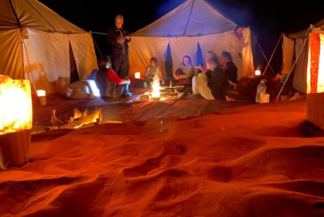Grain de Sable du Maroc - bivouac nomade sous une nuit étoilée dans le désert - groupe de personnes assis autour du feu de camp