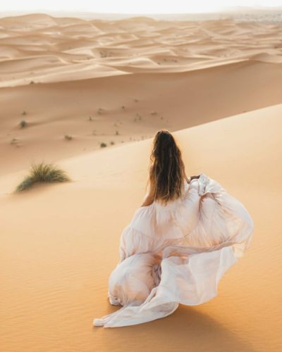 Portrait of bride woman in amazing wedding dress in Sahara desert, Morocco. Warm evening light, beautiful pastel tone, sand dunes on horizon. View from behind ? MARIAGE GRAIN DE SABLE? DESERT MAROC.